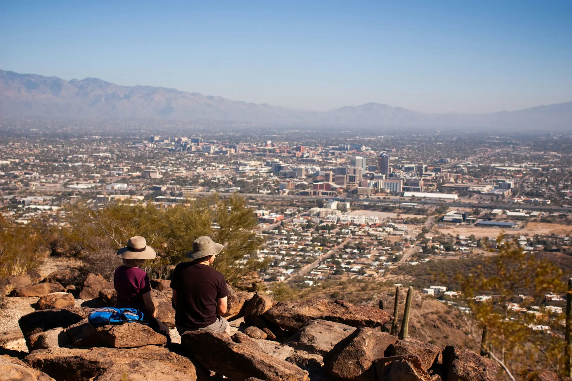 Two hikers rest at the peak of Tumama Hill overlooking scenic downtown Tucson, AZ.